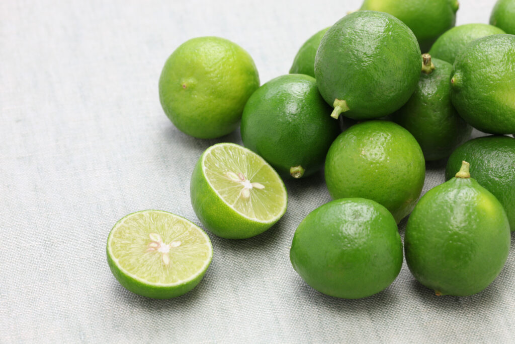 Fresh Key Limes piled together, with one lime cut open, showcasing their vibrant green interior. Perfect for producing Key Lime Juice Concentrate.