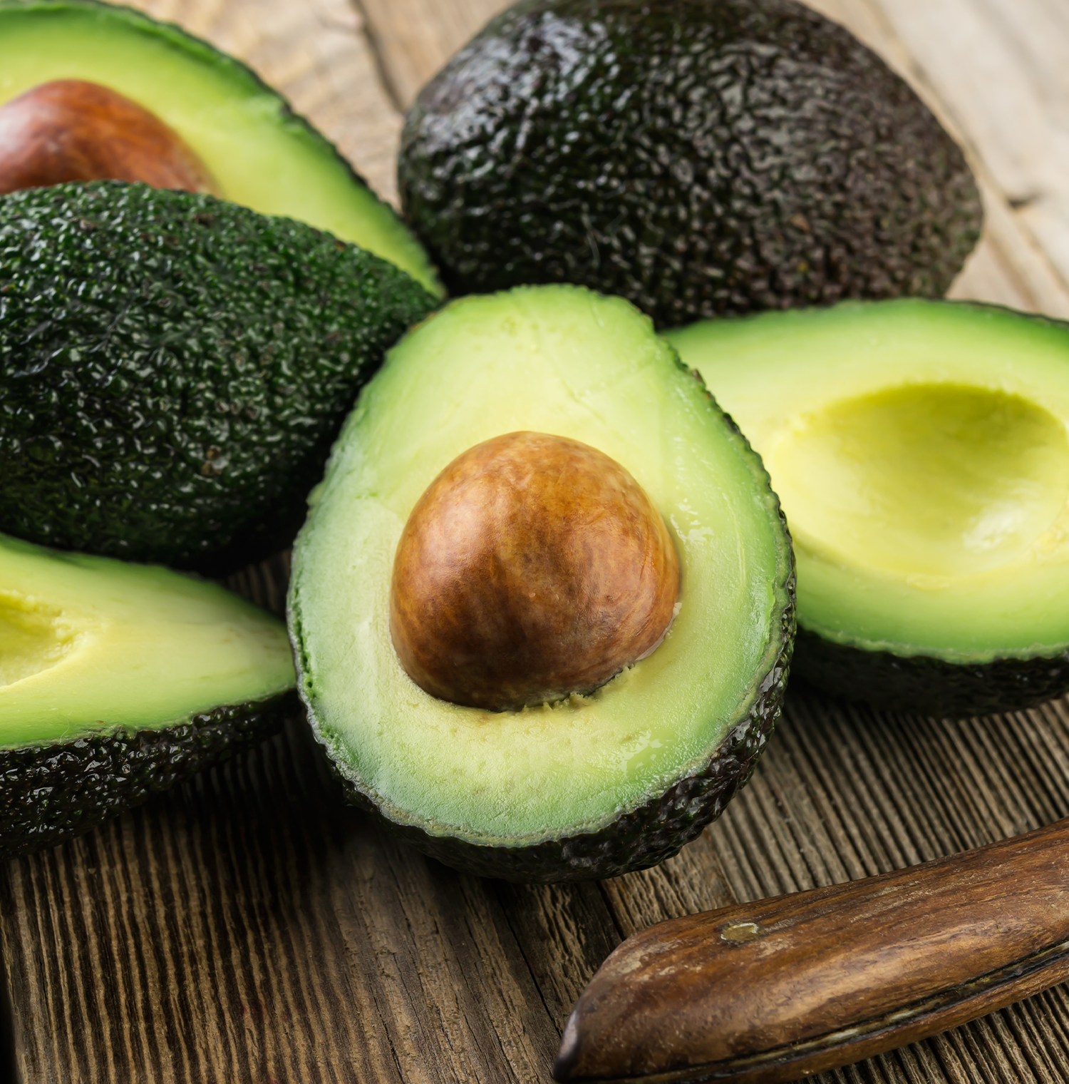 Several avocados, some cut in half on a wooden surface