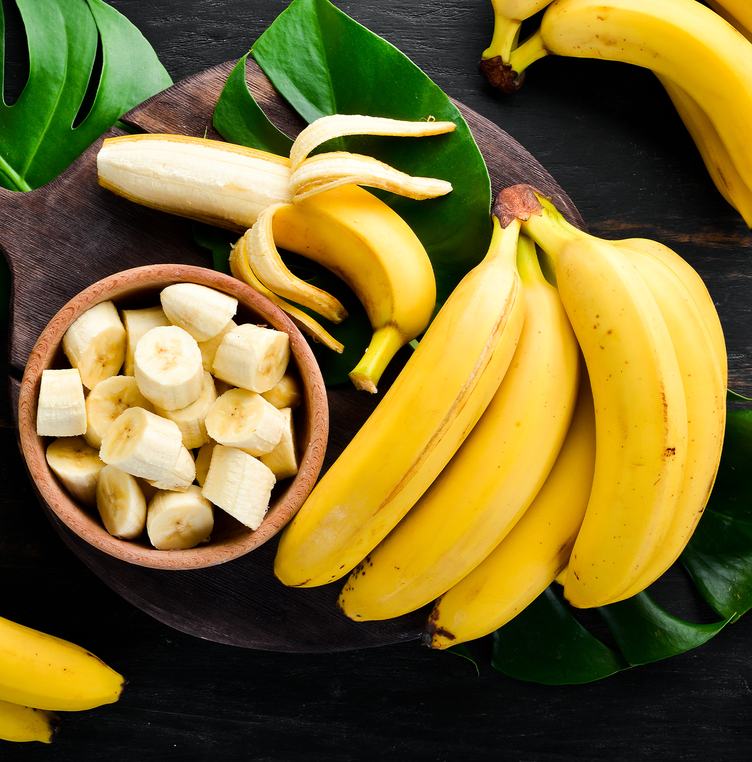 A bunch of bananas with a bowl of sliced bananas