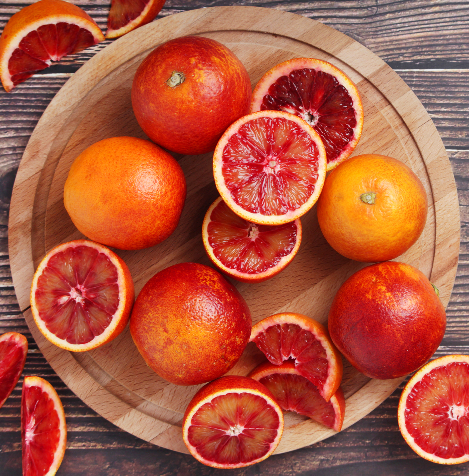 Blood oranges. Some are cut in half. Resting on a wooden board.