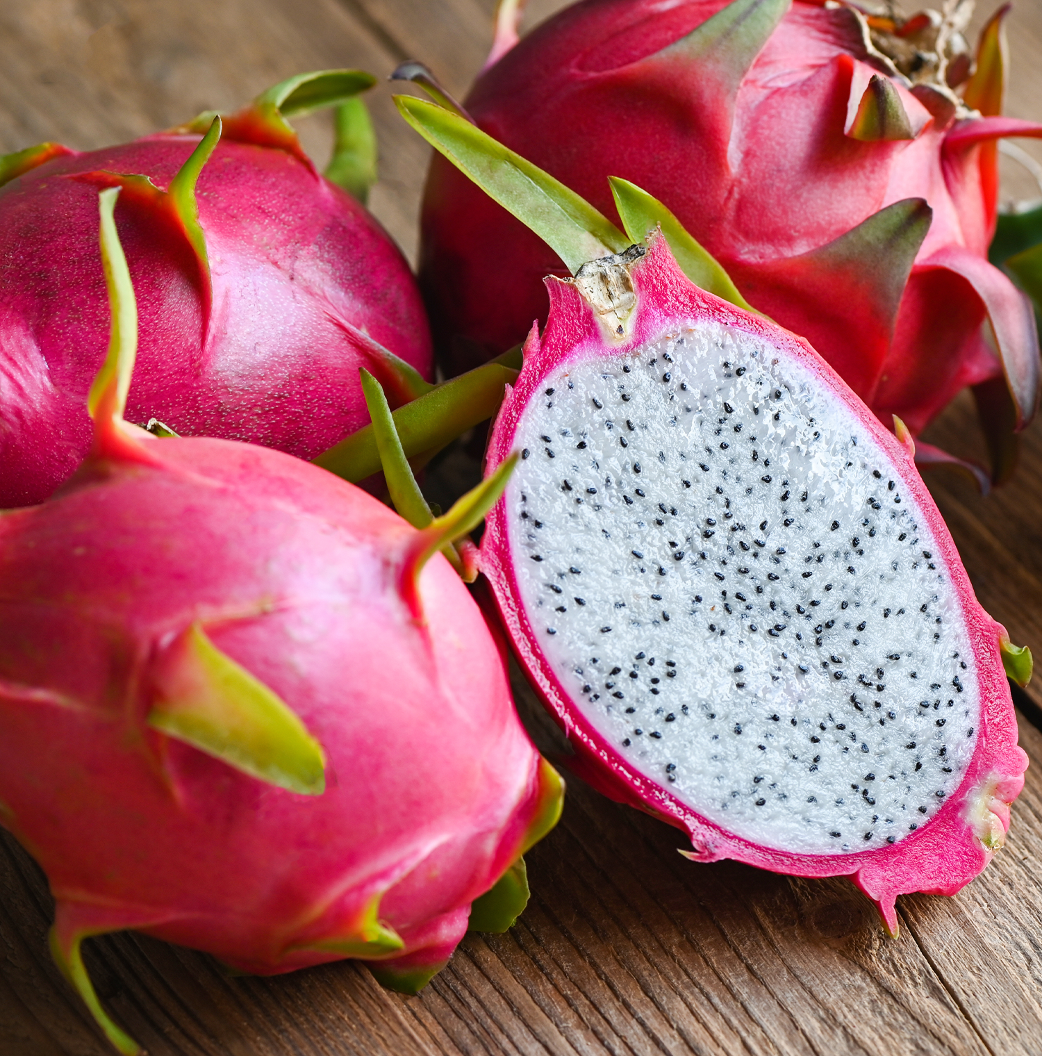 Four dragonfruits resting on a wooden surface. One is cut in half.