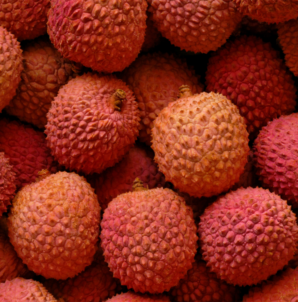 Close-up of fresh lychees with vibrant pink-red textured skin, showcasing the exotic fruit used to produce premium Lychee Puree.