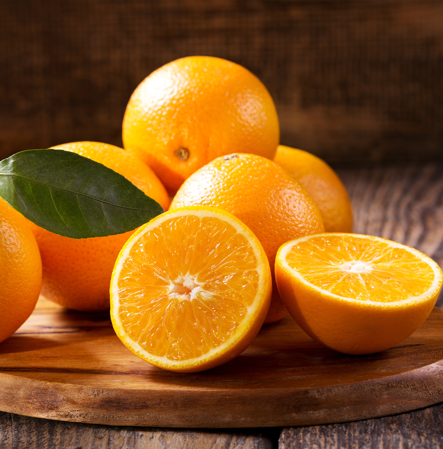 Close up image of oranges resting on a wooden surface. One is cut in half.