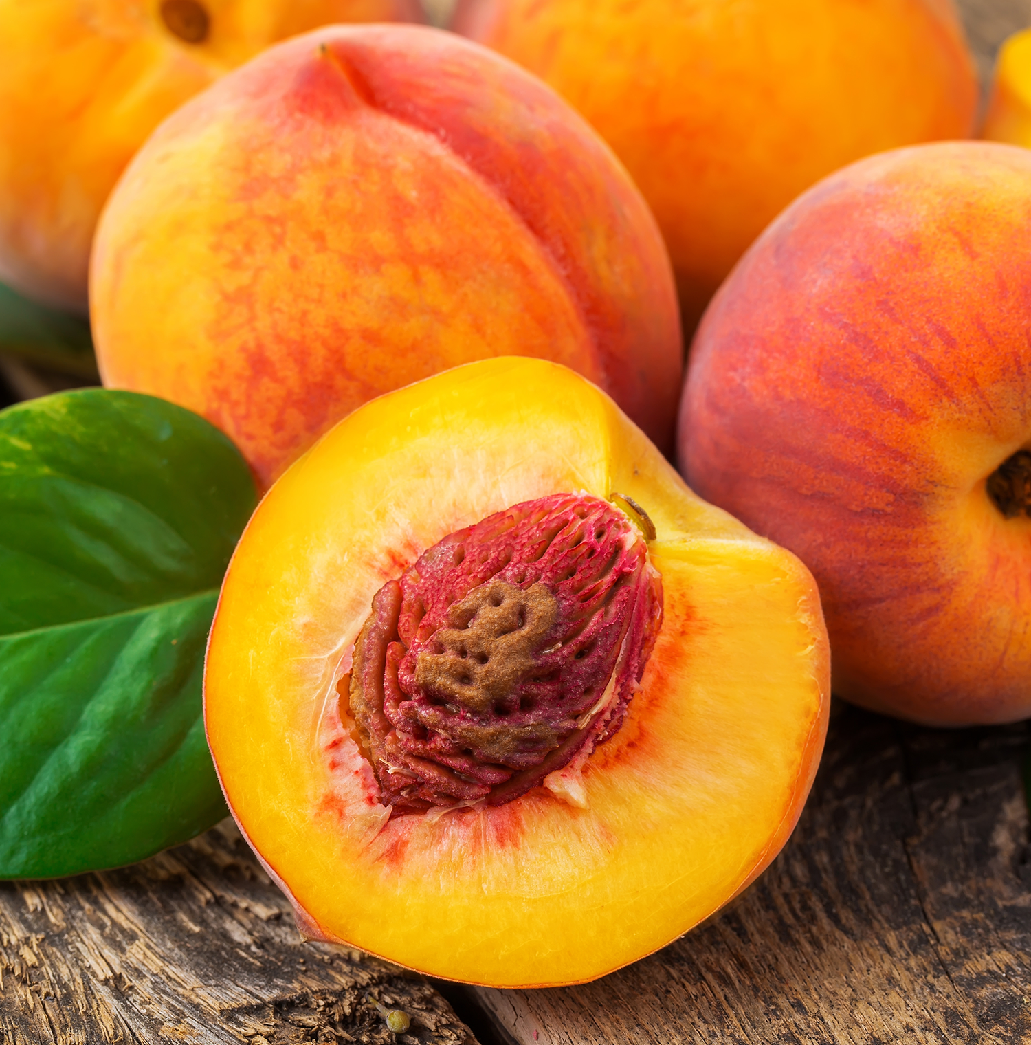 A close up image of peaches. One is cut in half, revealing the pit.