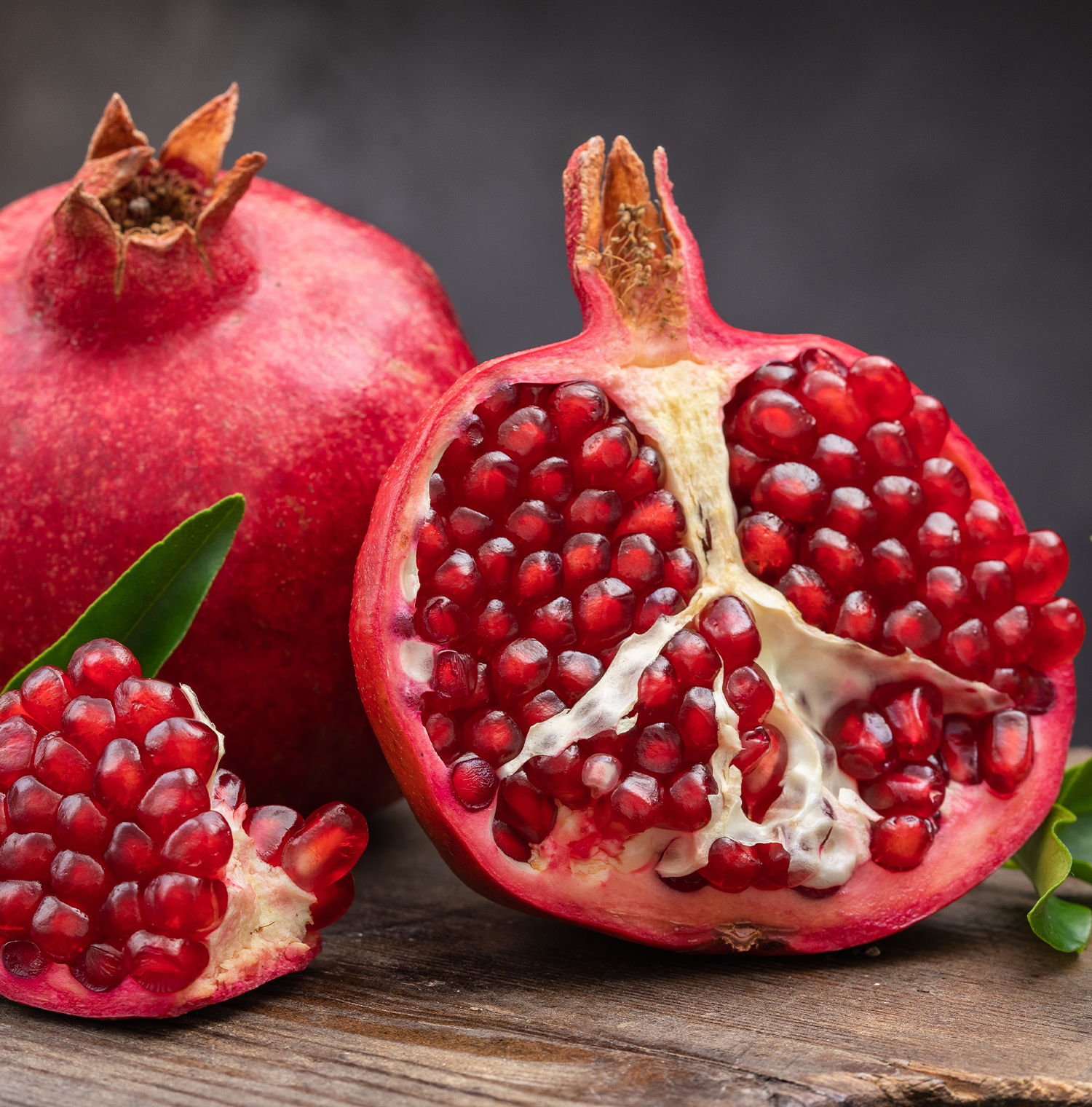 A close up image of pomegranates. One is cut in half, revealing the arils