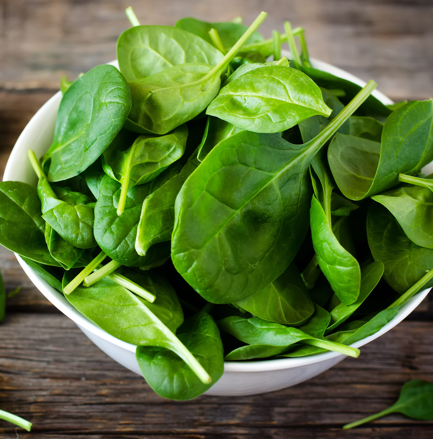 A white bowl full of spinach leaves on a wooden surface