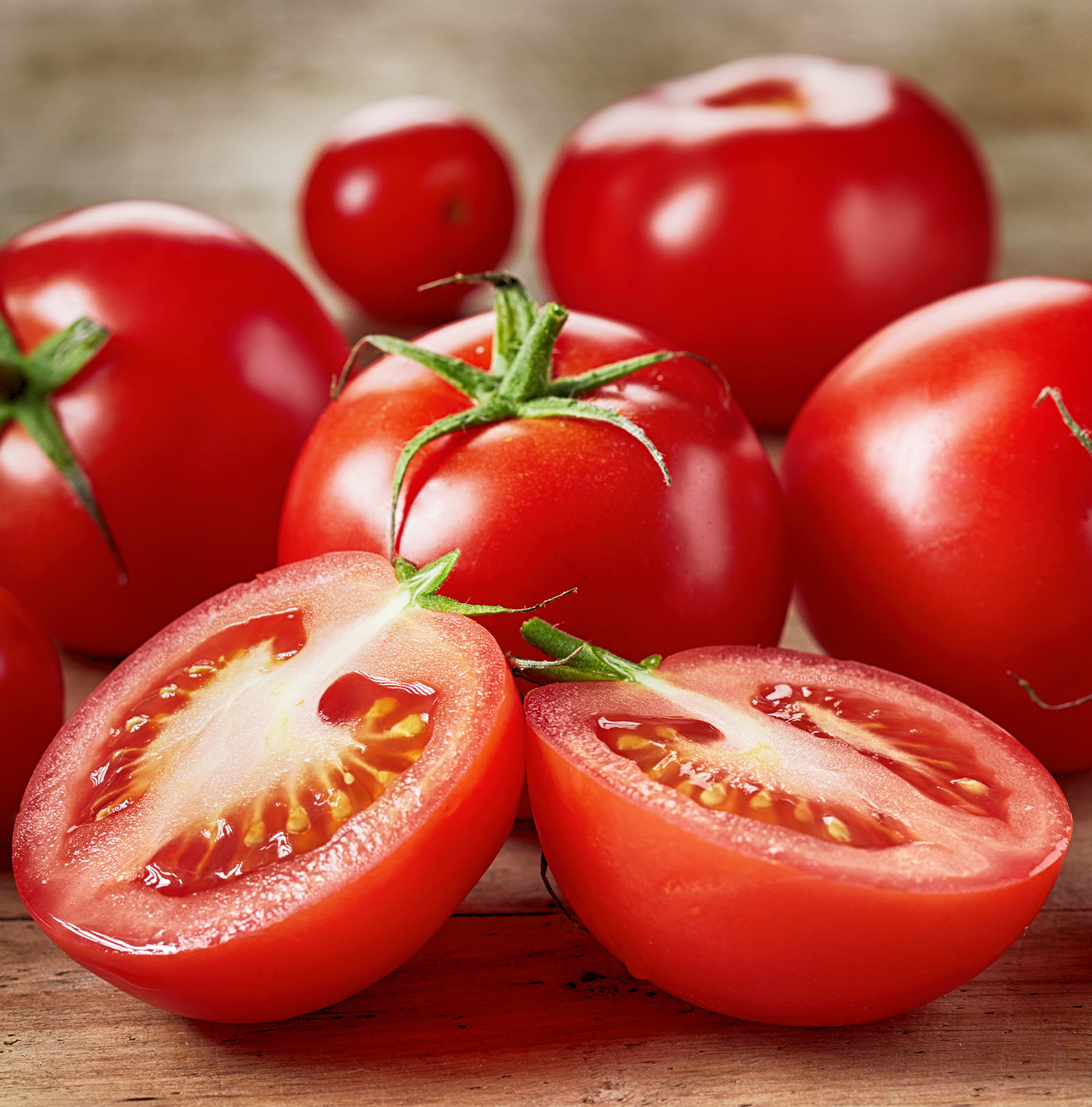 A close up image of tomatoes resting on a wooden surface. One is cut in half.