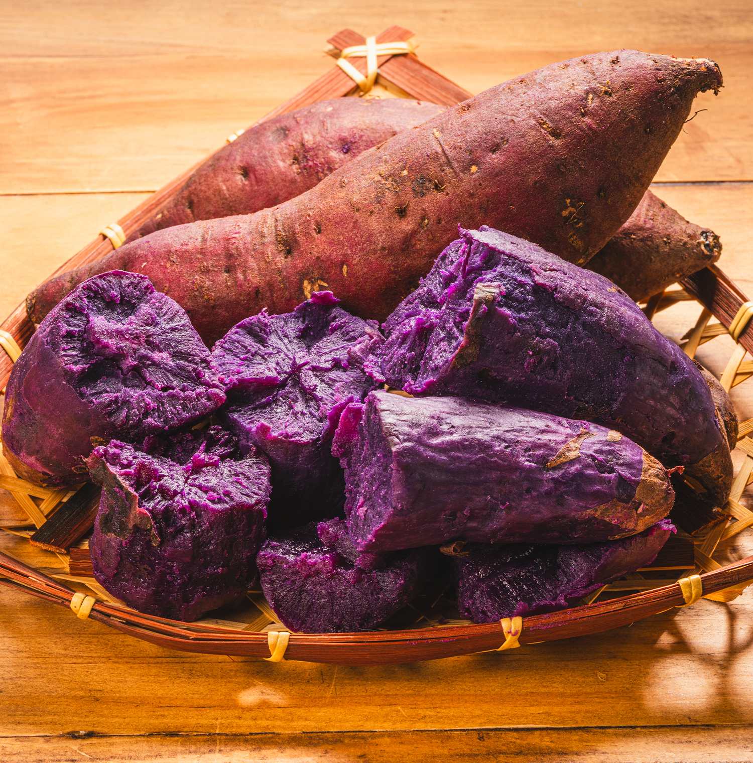 A wicker basket full of ube potatoes. One is peeled and looks to be cooked, revealing a bright purple flesh. There are some intact ube potatoes in the basket as well. 